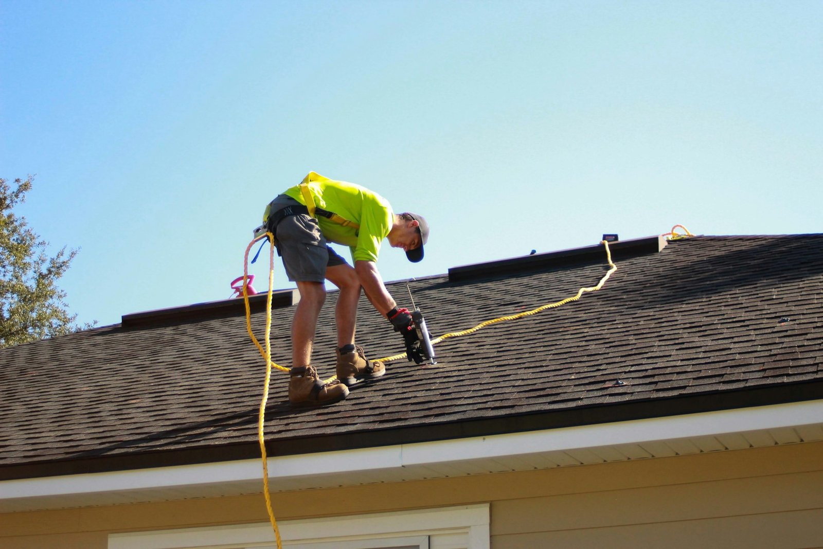 Professional roofer installing asphalt shingles with a power tool